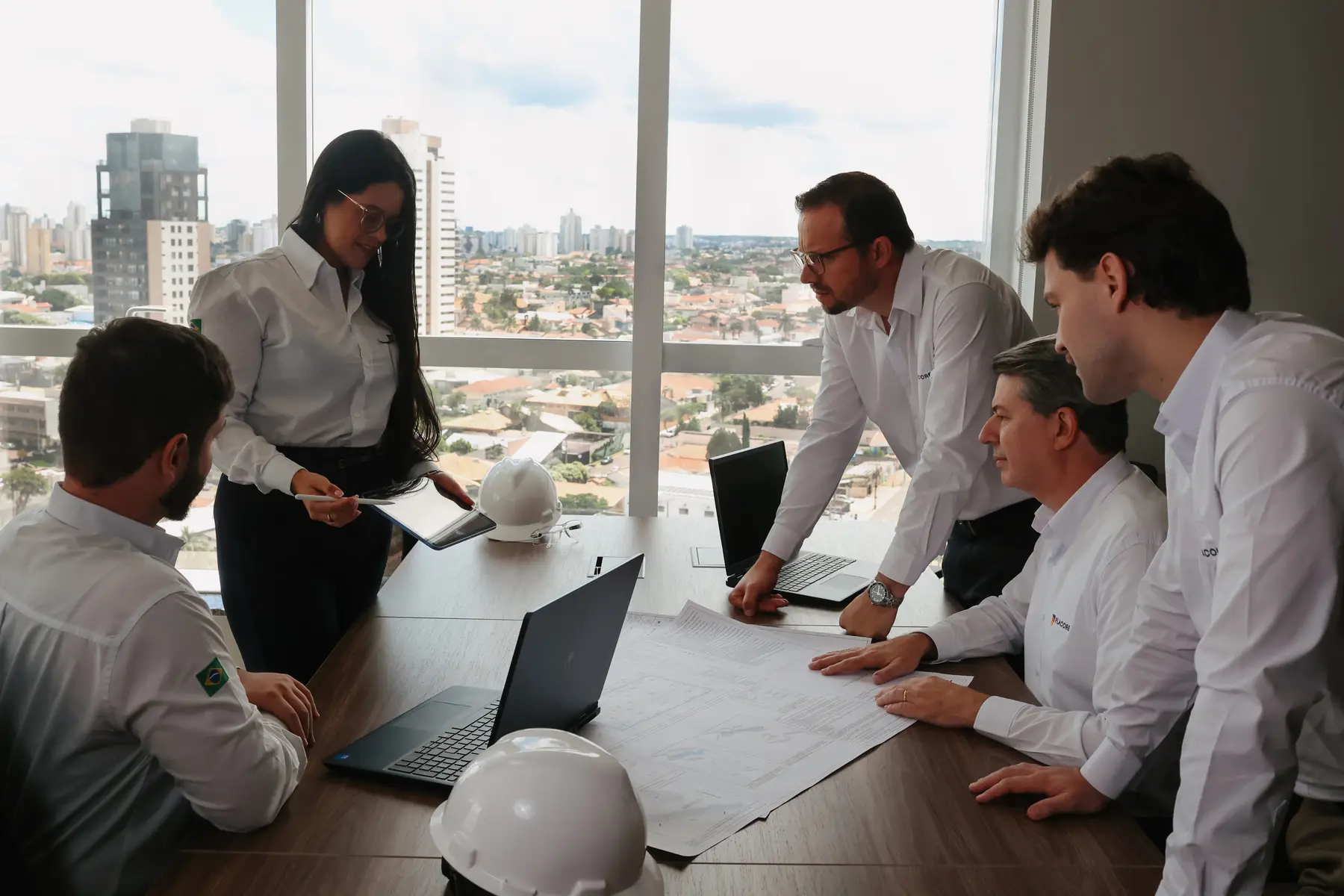 Equipe da Placore reunida em volta de plantas de engenharia, com capacetes sobre a mesa